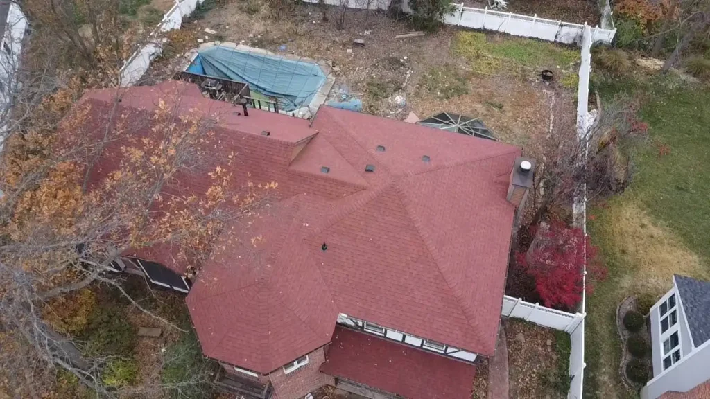 Aerial view of a brown roof with multiple peaks, surrounded by trees in autumn colors and an overgrown backyard.