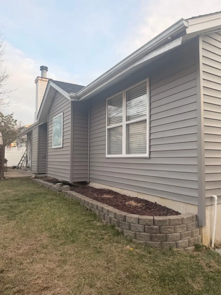 A side view of a modern home featuring grey siding, large windows, and a neatly landscaped yard with a stone border.
