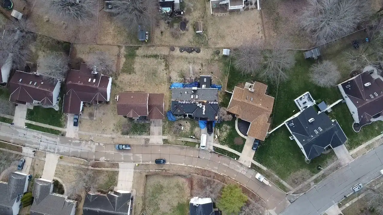 Aerial view of a residential neighborhood with several houses and yards, showing various roofs, green grass, and a curved street.